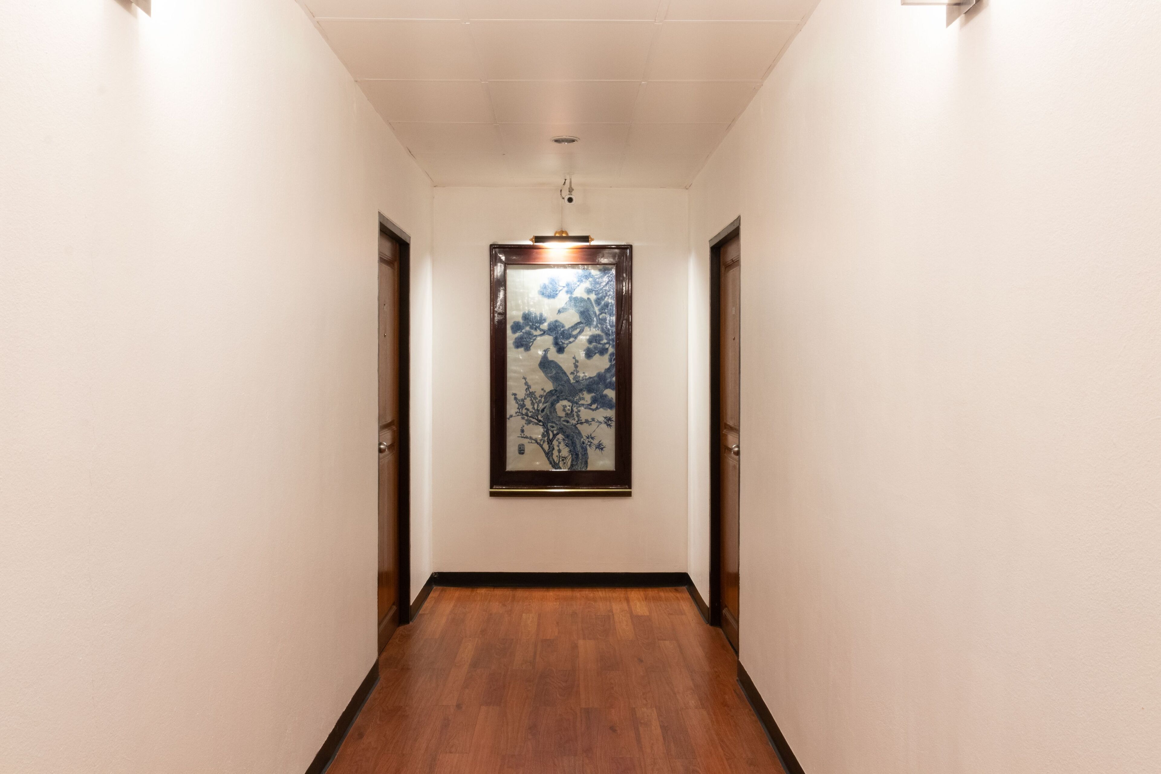 A hallway with wooden flooring, white walls, and a framed artwork on the wall.