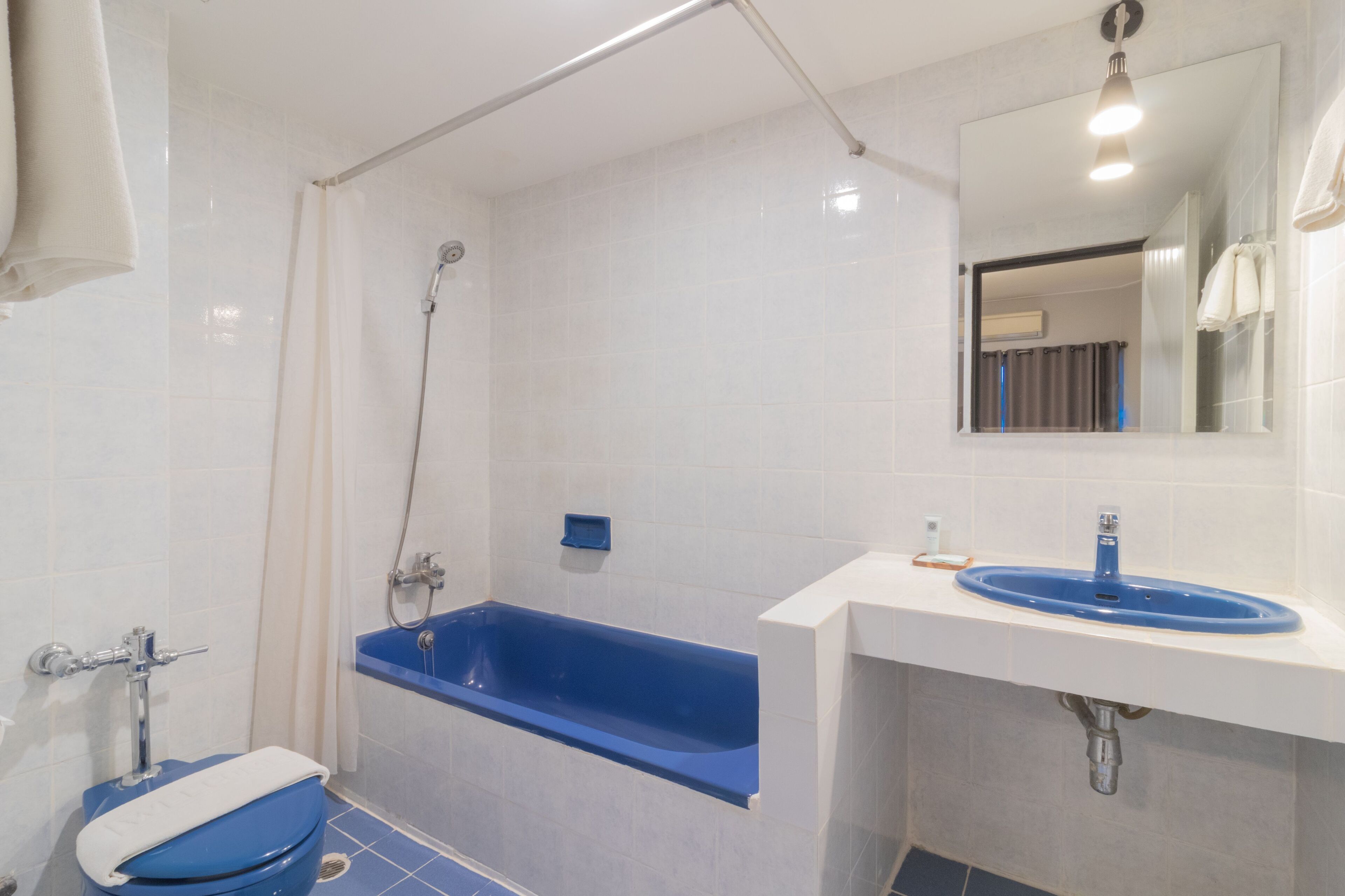 Un baño con una bañera azul, un lavabo blanco y un espejo sobre el lavabo.