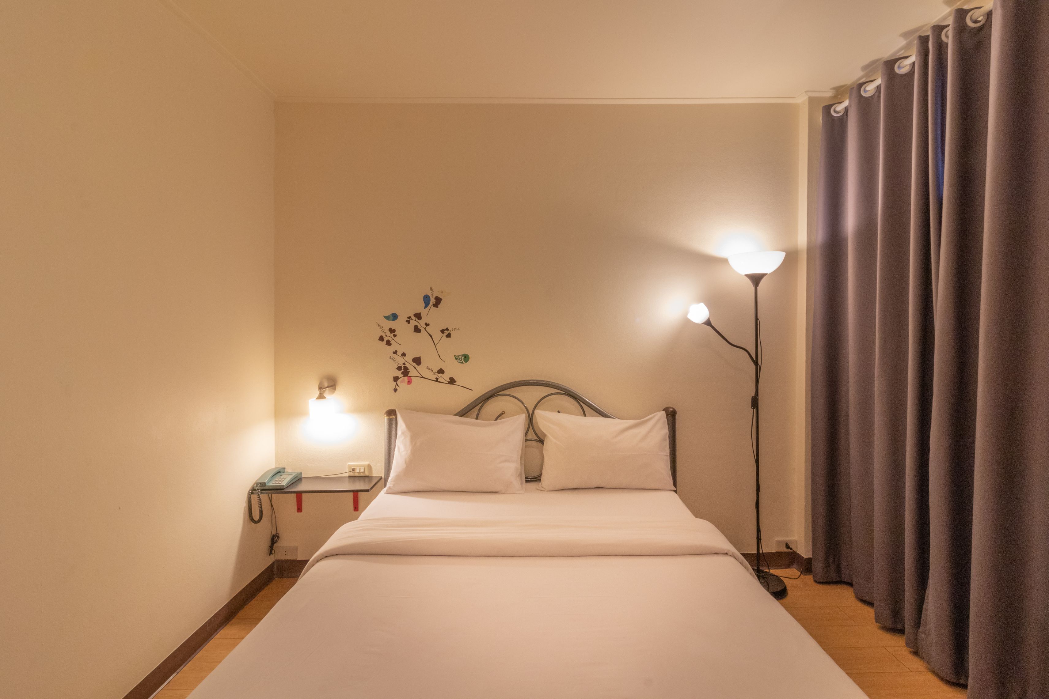 A neatly made bed with white linens, a bedside table with a lamp, and a wall-mounted telephone.