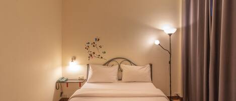 A neatly made bed with white linens, a bedside table with a lamp, and a wall-mounted telephone.