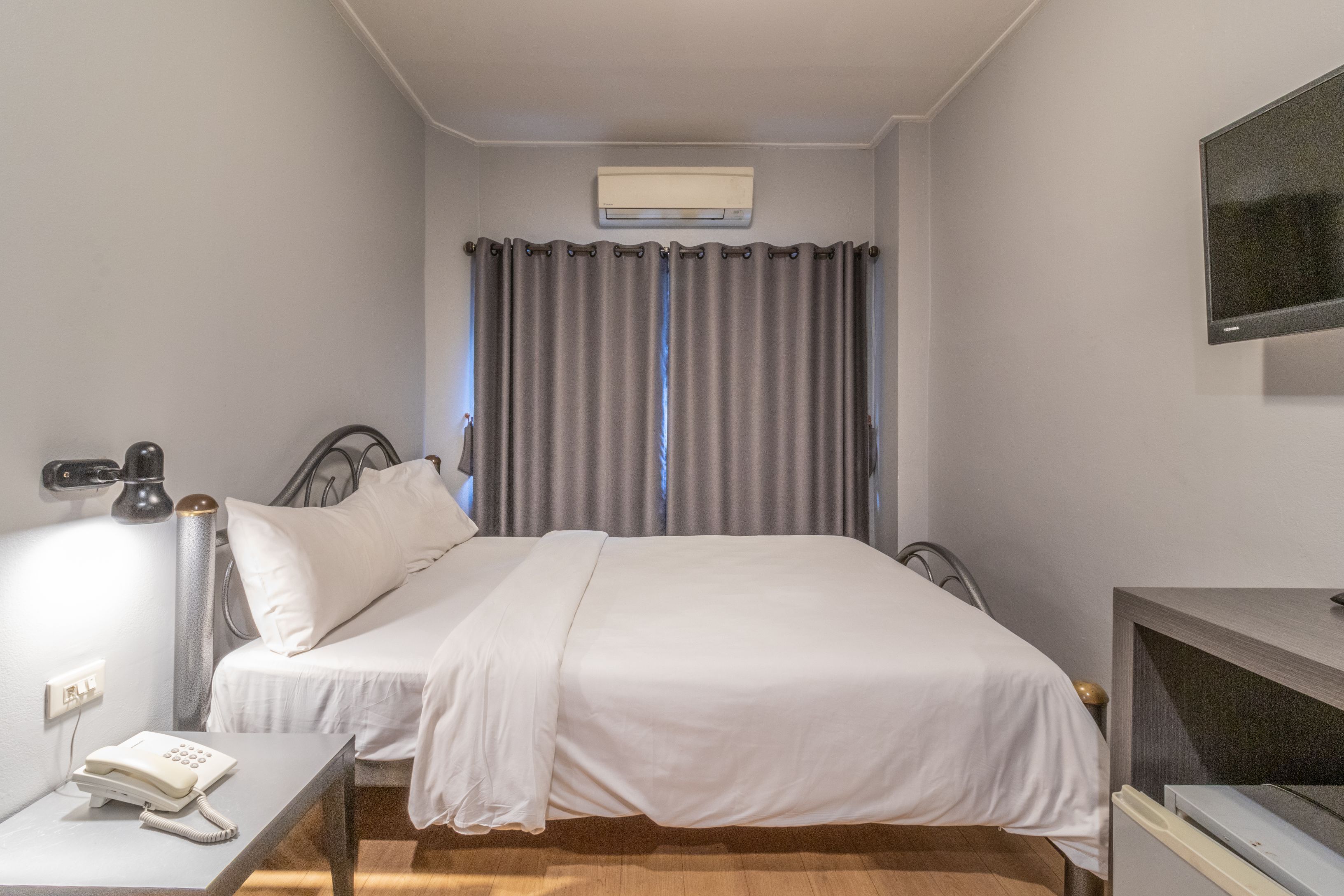 A hotel room with a bed, bedside table, lamp, and a mounted television.