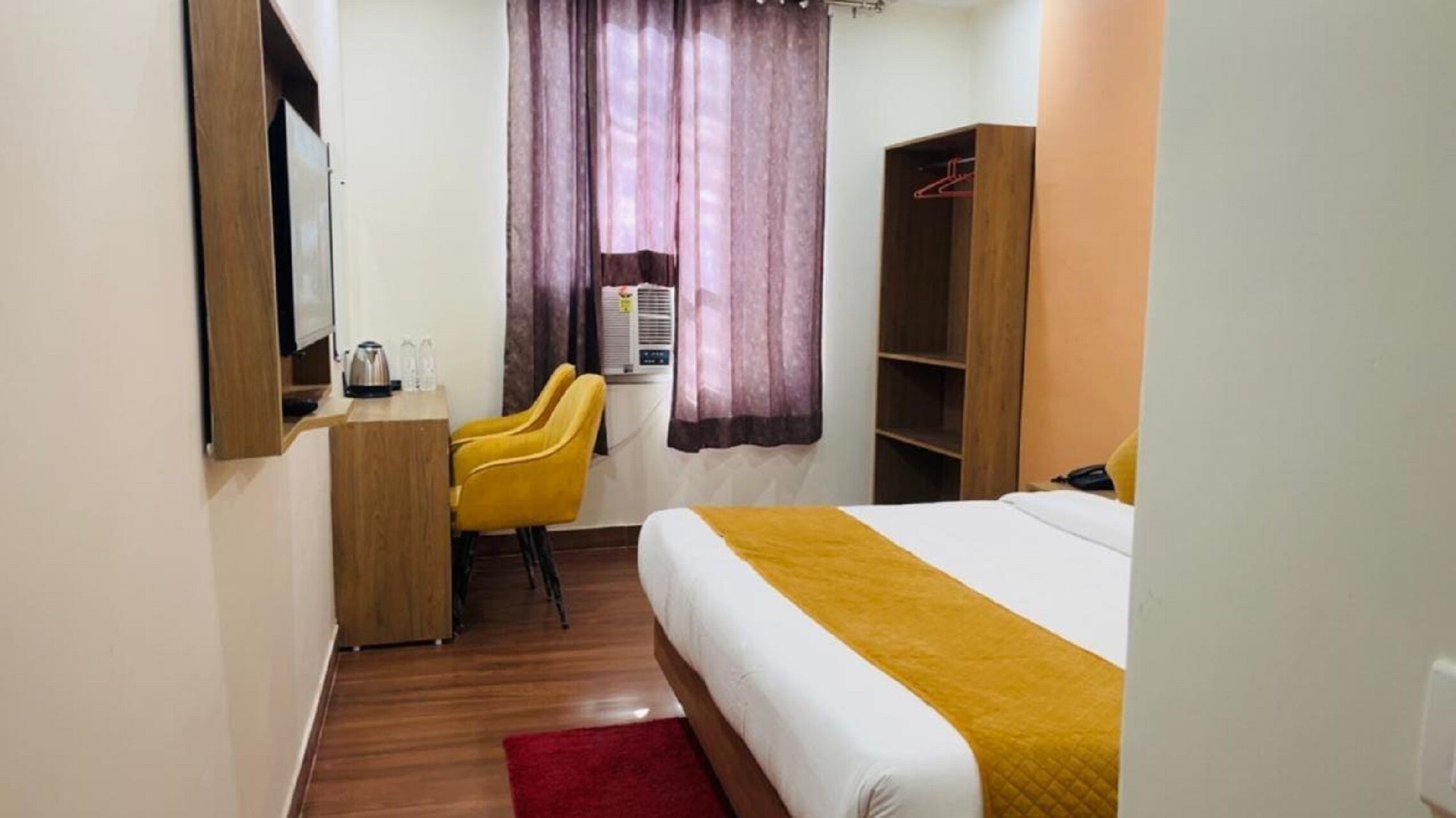 A hotel room with a bed, a desk with a chair, a wardrobe, and a window with curtains.