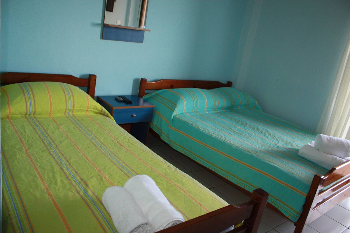 A twin room with two single beds, each with a different patterned bedspread, a nightstand with a phone, and a folded towel on the bed.
