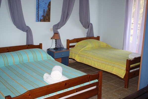 Dos camas de madera con ropa de cama a rayas, una mesita de noche con lámpara y un cuadro en la pared.