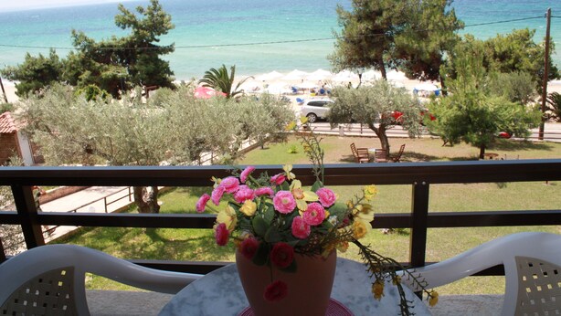 A balcony with a potted plant, a view of the beach, and a clear sky. - Villa Bambola (Nea Propontida)