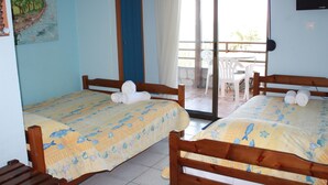 A room with two wooden beds, each with a yellow bedspread featuring sea creatures. There is a painting on the wall, a sliding glass door leading to an outdoor area with a table and chairs. - Villa Bambola (Nea Propontida)
