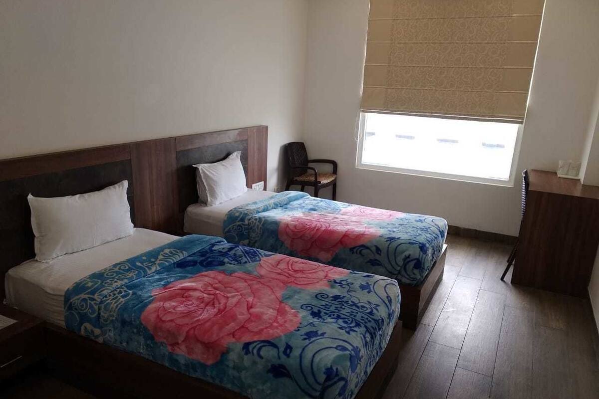 A hotel room with two beds, a window with blinds, a chair, and a desk.