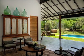 A covered outdoor seating area with a pool, chairs, and a wooden cabinet with glass doors. - Nyne Hotels Mayur Lodge - Yala (Thissamaharama)