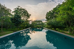 A rectangular swimming pool with clear water reflecting surrounding trees and sky. - Nyne Hotels Mayur Lodge - Yala (Thissamaharama)
