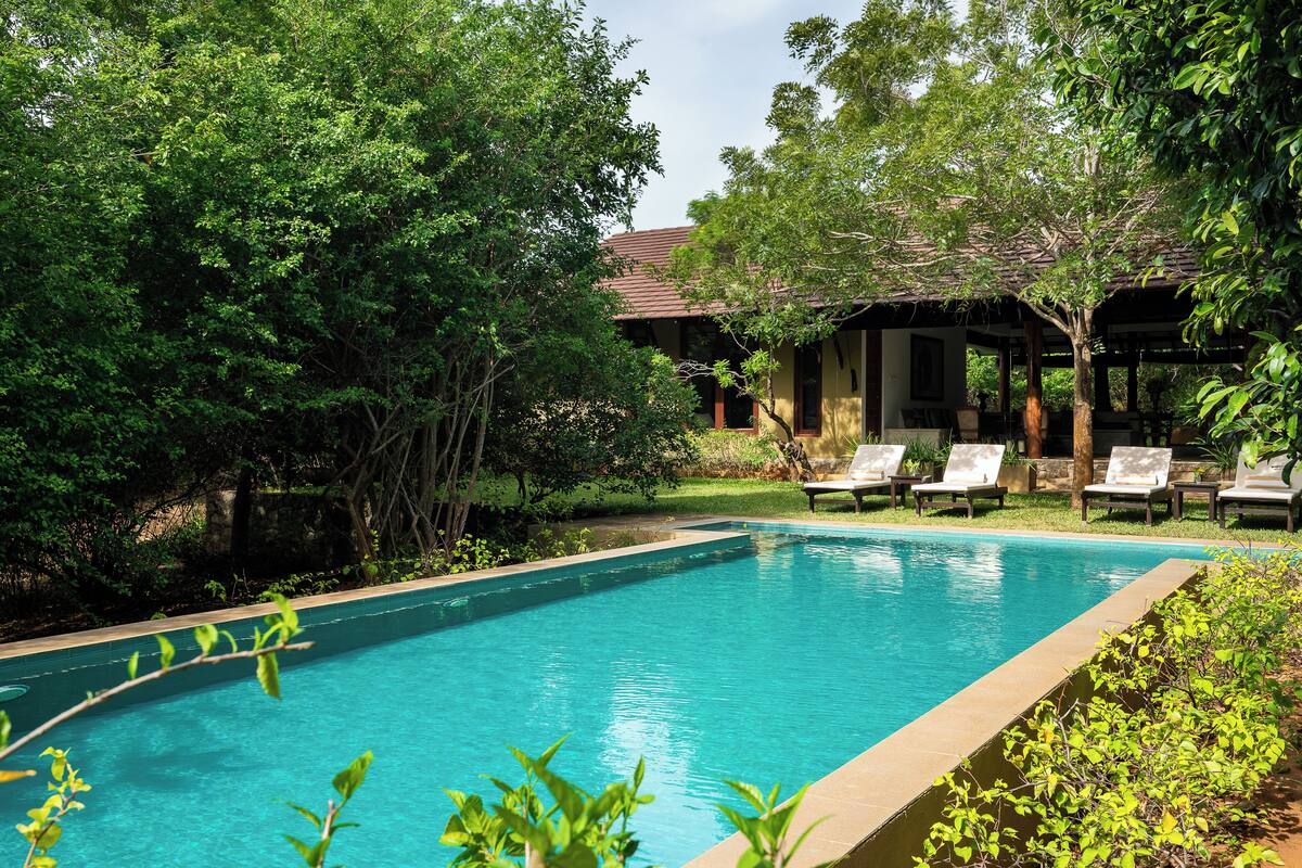 A swimming pool surrounded by lush greenery and a building with a tiled roof.