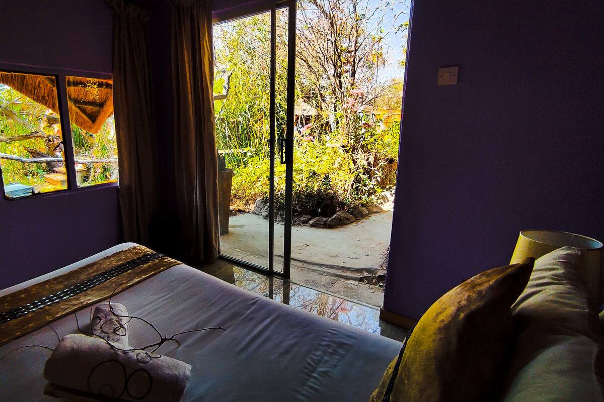 A bedroom with a bed, a window, and a view of a garden.