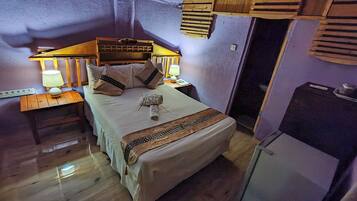 A cozy bedroom with a wooden headboard, two bedside lamps, a bed with a white bedspread and decorative pillows, a small table with a lamp, and a wooden nightstand.
