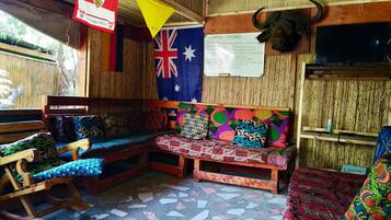 A rustic room with a wooden bench, colorful cushions, a wall-mounted TV, and a flag.