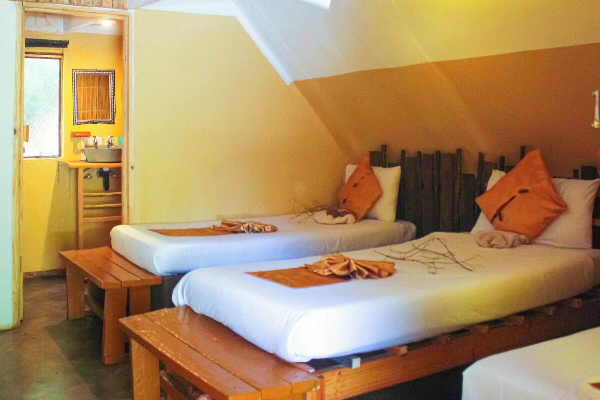 A cozy bedroom with two single beds, a wooden bench, and a small kitchenette.