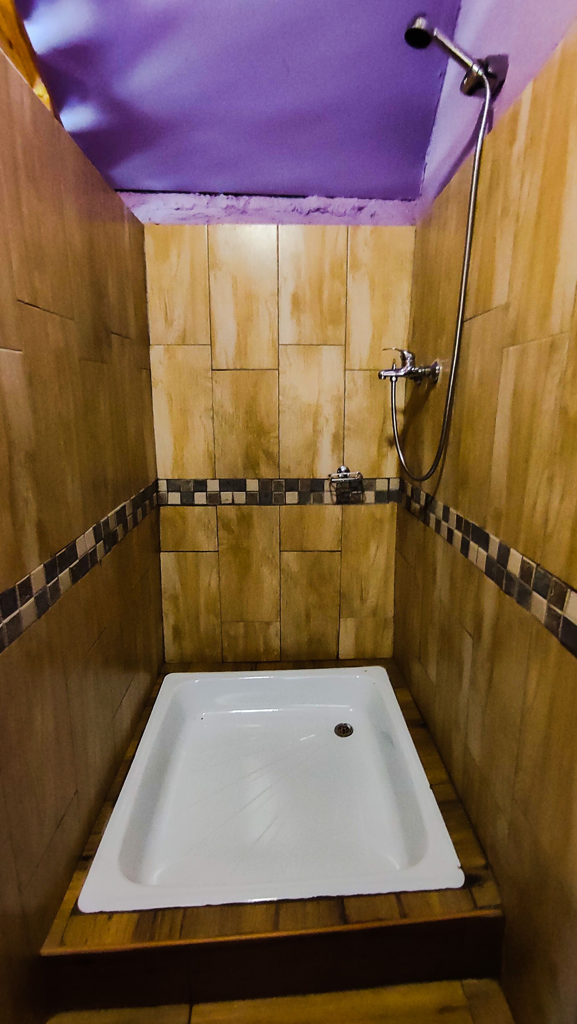 Une petite baignoire carrée, dotée d’un pommeau de douche, entourée de murs en bois et posée sur un sol carrelé.