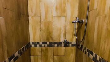 Une petite baignoire carrée, dotée d’un pommeau de douche, entourée de murs en bois et posée sur un sol carrelé.