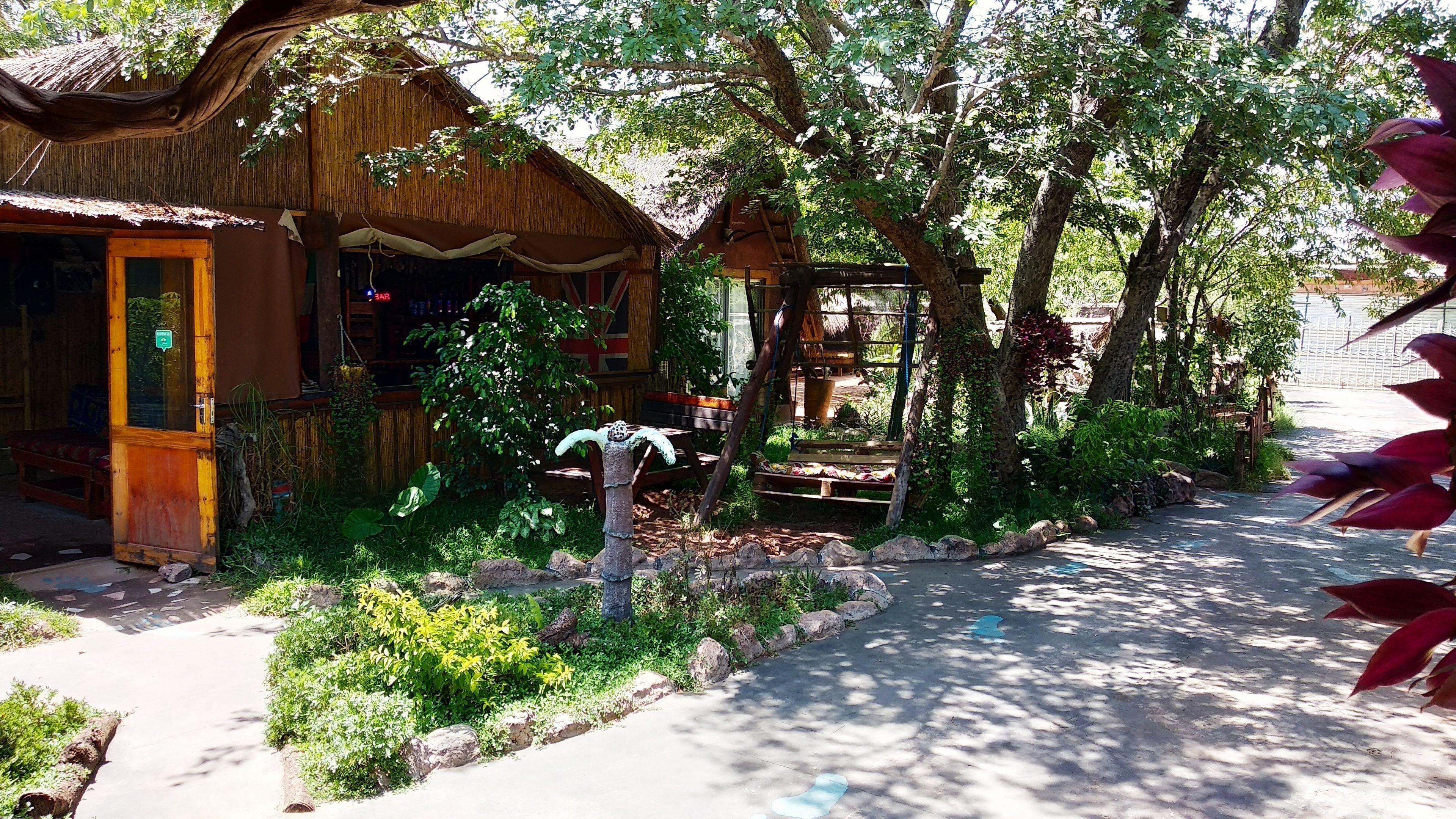 A rustic building with a thatched roof, surrounded by lush greenery and a paved pathway.