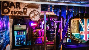 Zona de bar con un letrero de neón, un refrigerador lleno de bebidas y una bandera del Reino Unido.