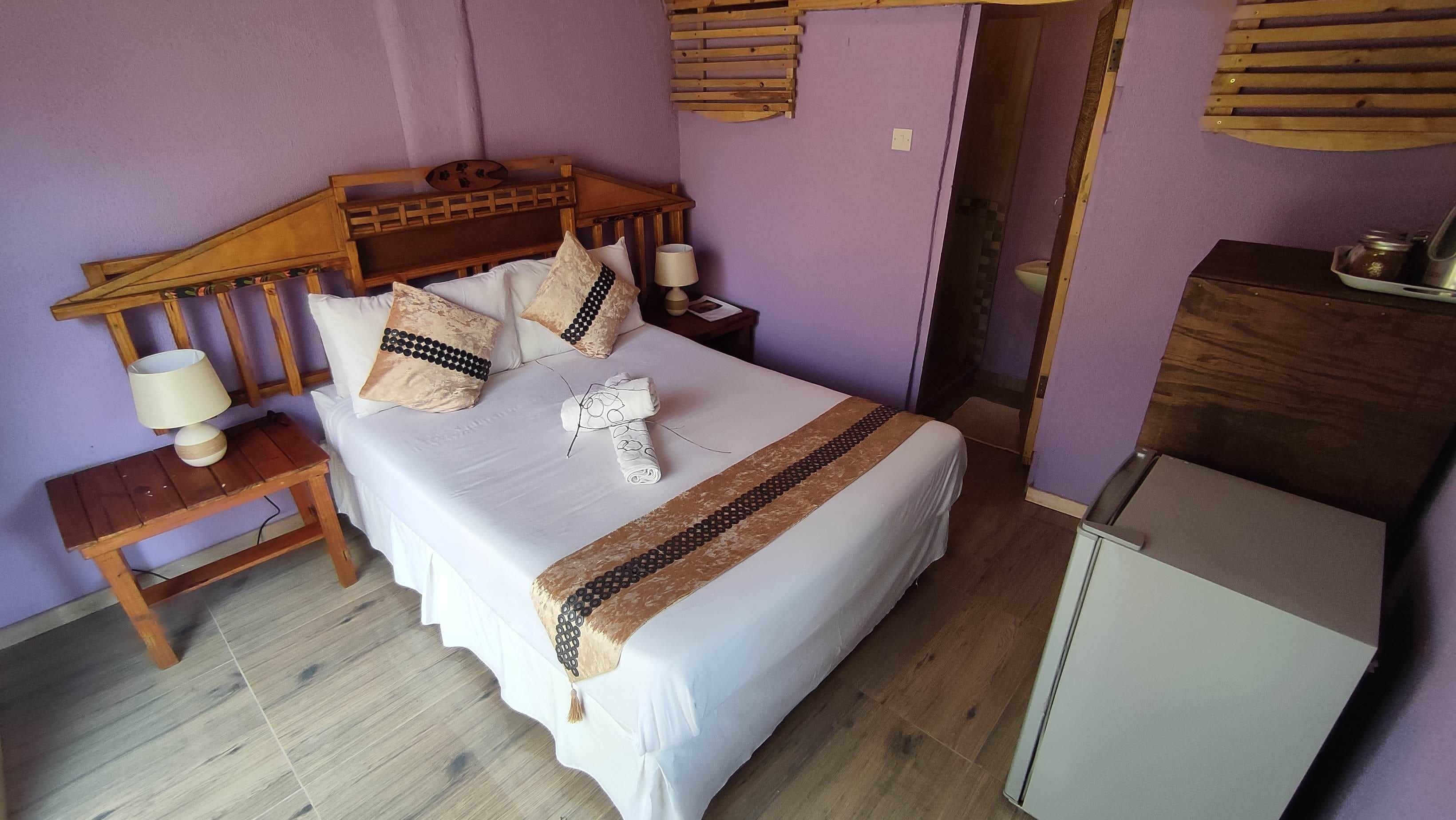 A neatly made bed with a wooden headboard, a bedside table with a lamp, and a small cabinet.