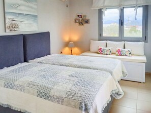 A bedroom with two beds, a window with a view, and a wall with framed pictures. - Elegant Maisonette Garden near Beach (Aegina)