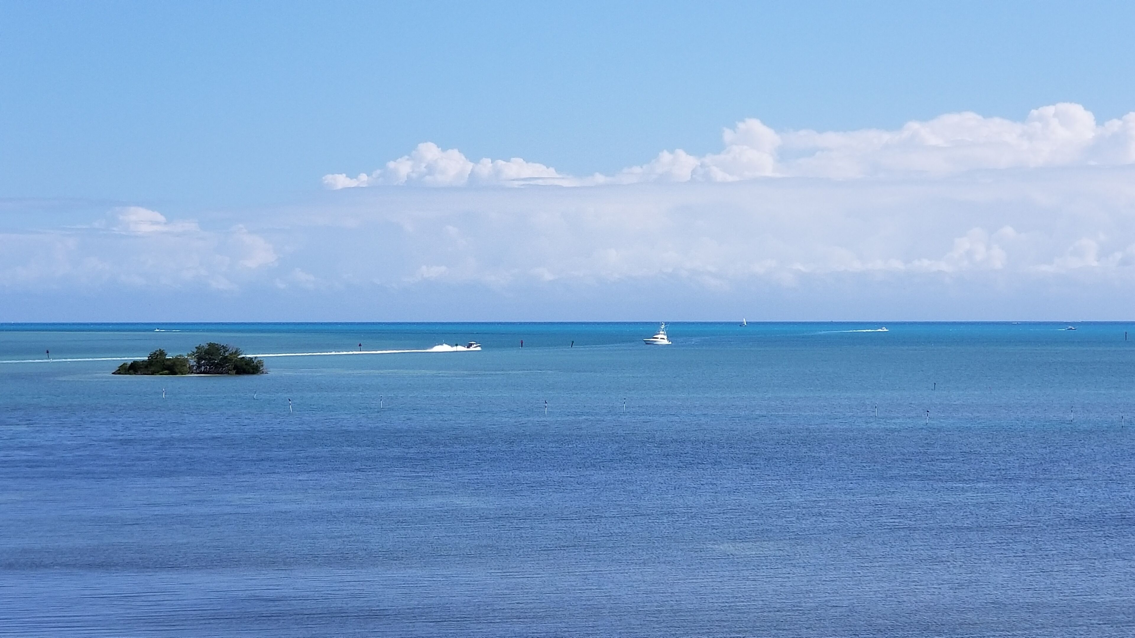 Vista costiera con acque calme, una piccola isola e una vela in lontananza.