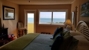 A bedroom with a bed, a chair, a nightstand, a lamp, and a window with a view of the sea. - SPECTACULAR OCEANFRONT VIEWS , FREE WIFI, HD SMART TV'S, SUMMER SPECIAL RATES (Tavernier)