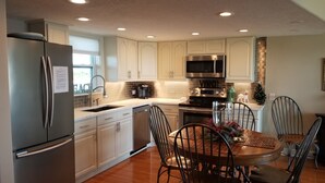 A modern kitchen with stainless steel appliances, white cabinetry, and a dining area with metal chairs. - SPECTACULAR OCEANFRONT VIEWS , FREE WIFI, HD SMART TV'S, SUMMER SPECIAL RATES (Tavernier)