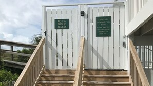 A set of wooden stairs leading to a gated area with two signs indicating private access and a notice for a swimming pool.