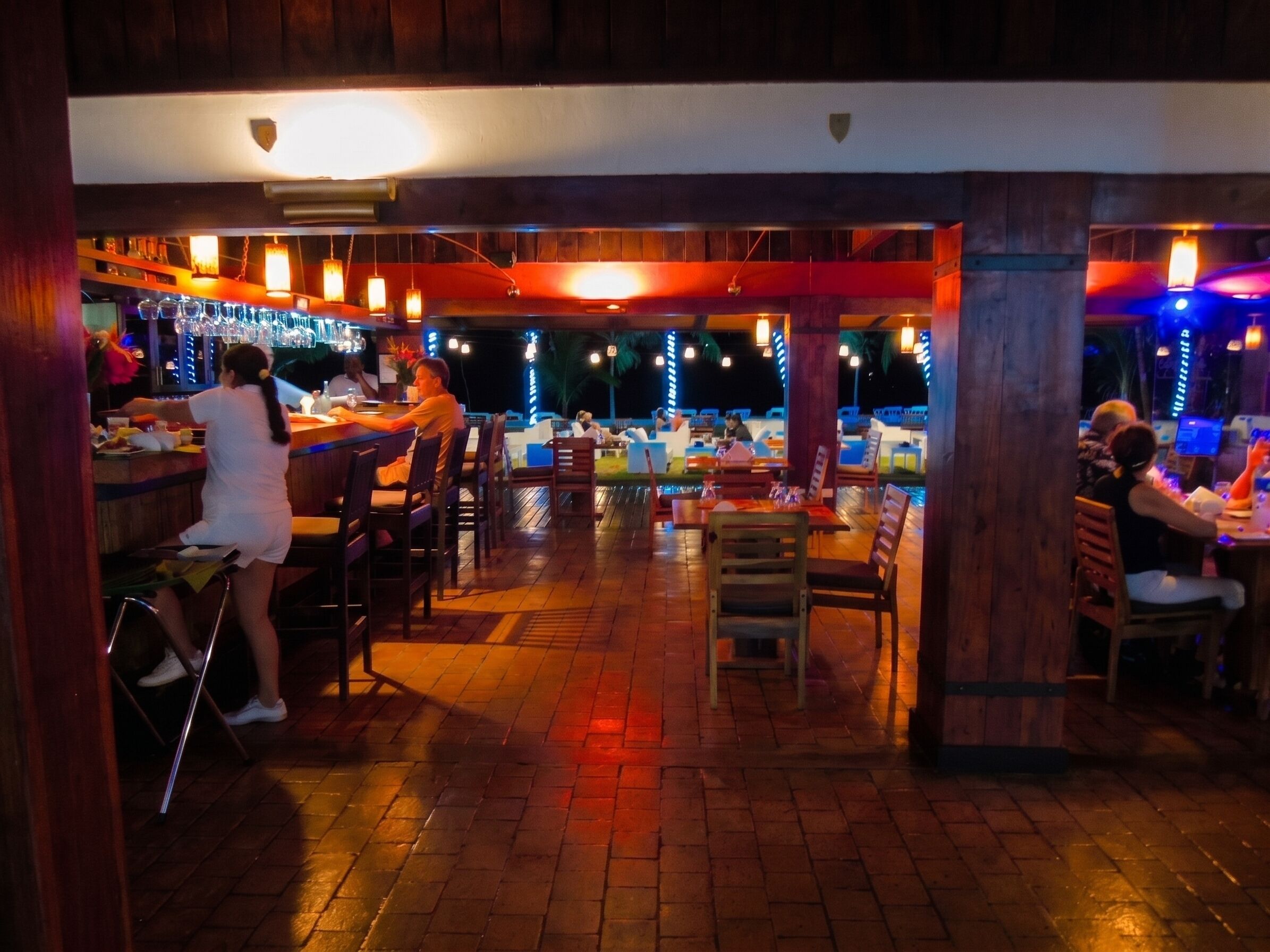 An indoor bar area with tables and chairs, a bar counter, and hanging lights.