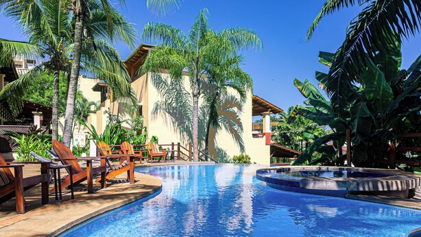 Piscina com espreguiçadeiras e palmeiras, cercada por edifícios.