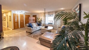 A spacious living room with a sofa, a coffee table, and a large plant. There are wooden doors and a chandelier. - We weathered Helene beautifully!      Welcome to your new, lovely mountain home! (Asheville)