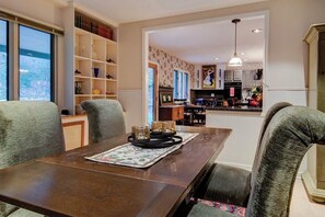 A dining area with a wooden table, cushioned chairs, and a bookshelf. - We weathered Helene beautifully!      Welcome to your new, lovely mountain home! (Asheville)