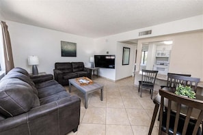A living room with a sofa, a coffee table, a TV, and a dining area with chairs and a table. - 140 Fully Furnished Vacation Rental with Resort Amenities (Scottsdale)