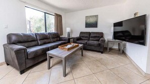 A living room with a sofa set, a coffee table, a TV, and a window with curtains.