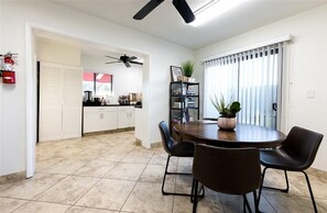 A dining area with a round table, four chairs, a ceiling fan, a bookshelf, and a window with blinds. - 140 Fully Furnished Vacation Rental with Resort Amenities (Scottsdale)