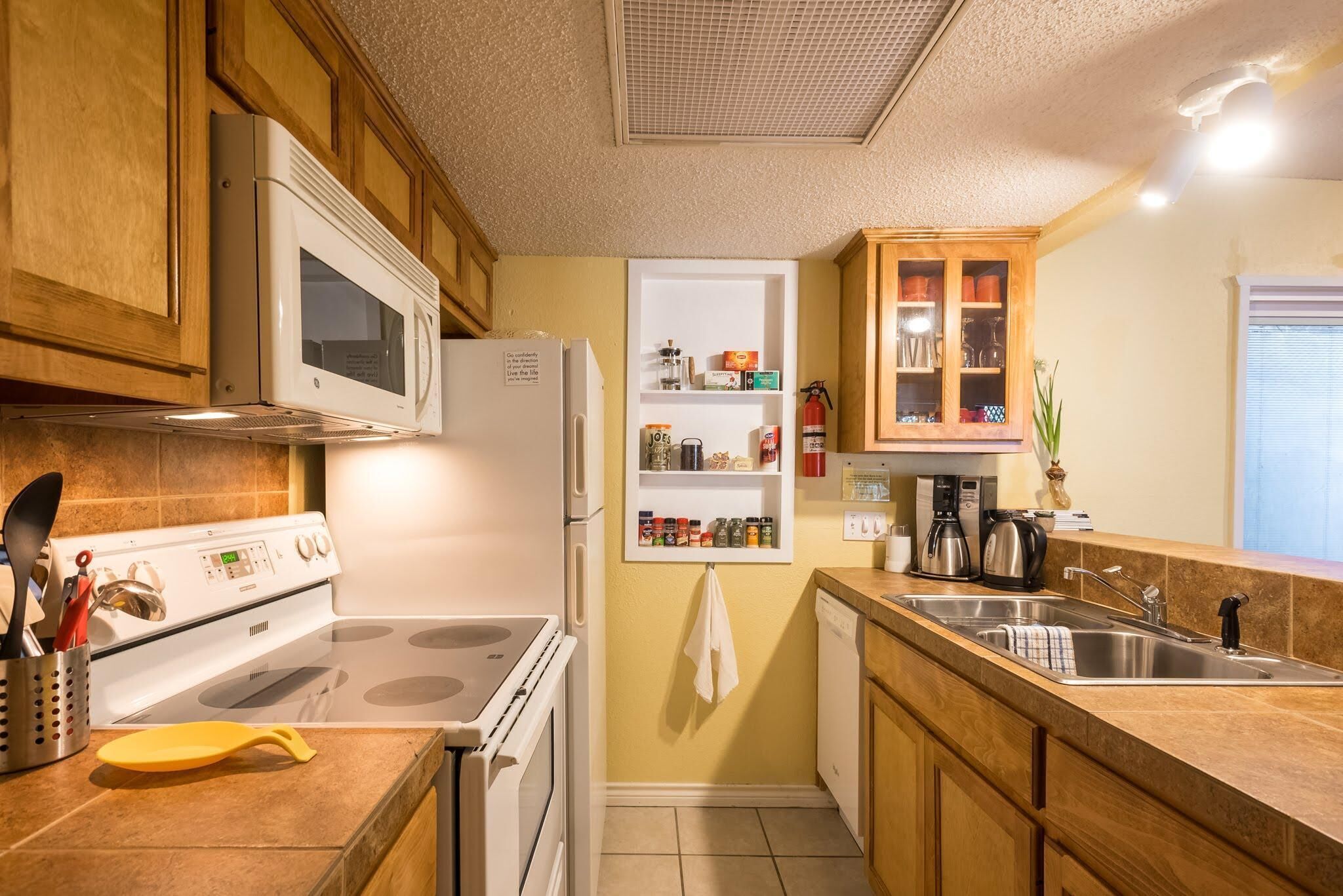 A kitchen with wooden cabinets, a white stove, a microwave, a coffee maker, and a sink.