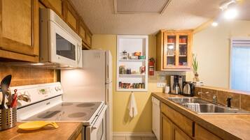 A kitchen with wooden cabinets, a white stove, a microwave, a coffee maker, and a sink.