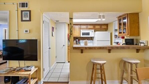Eine kompakte Küche mit Mikrowelle, Herd und Kühlschrank, eine kleine Bar mit Hockern und ein Fernseher auf einem Holzständer.