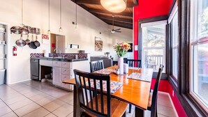 A modern kitchen with a dining area, featuring a wooden table, chairs, and a red accent wall. - Accessible Duplex Walking Distance to Park, Springs & Trails (Austin)