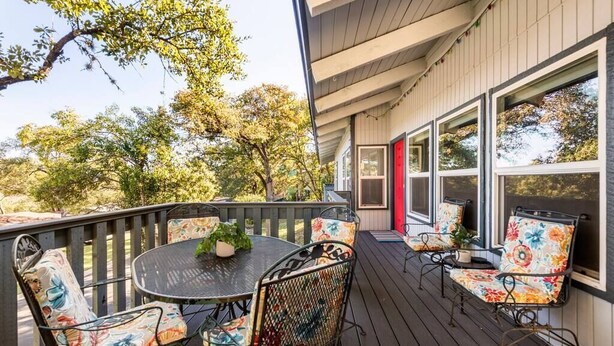 A covered outdoor seating area with a round table and chairs, a red door, and large windows. - Accessible Duplex Walking Distance to Park, Springs & Trails (Austin)