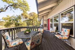 A covered outdoor seating area with a round table and chairs, a red door, and large windows.