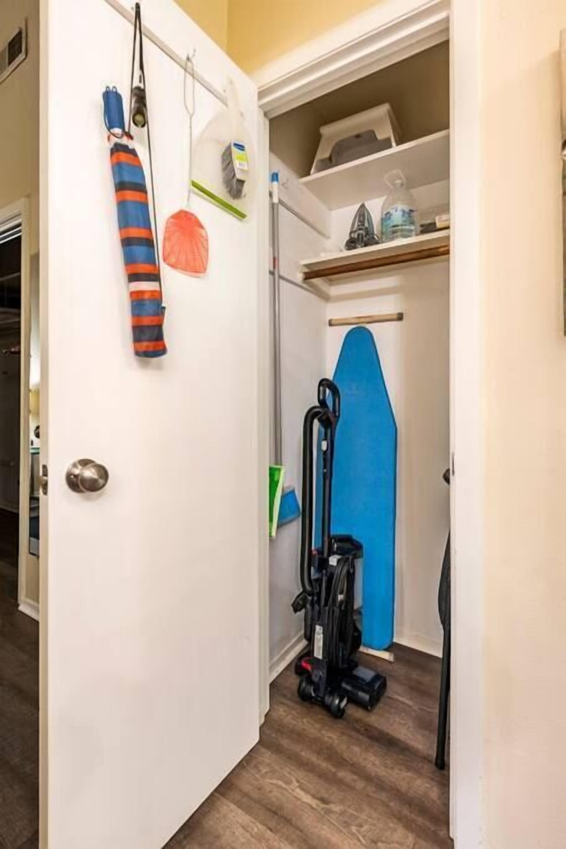 A narrow hallway with a vacuum cleaner, a blue mat, and some cleaning supplies on shelves.