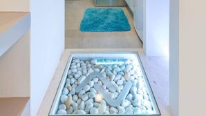 Ein schmaler Flur führt zu einer Küche mit einer türkisfarbenen Arbeitsplatte und einem Glasaquarium mit Kieselsteinen.