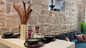 Ein Essbereich mit Steinwänden, einem weißen Tisch, schwarzen und grünen Schalen, einer dekorativen Vase und einer grünen Pflanze.