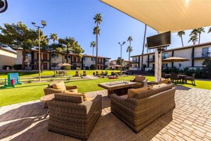 An outdoor patio with wicker furniture, a flat-screen TV, and a well-maintained lawn.