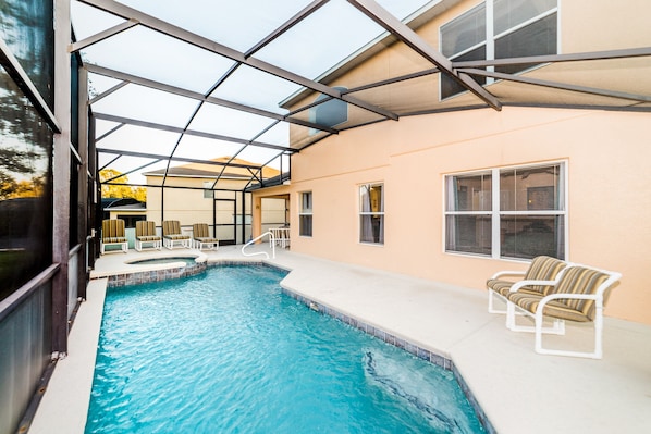 A swimming pool with a glass enclosure, lounge chairs, and a patio area.