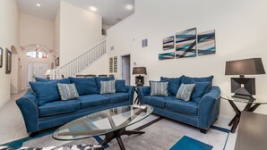 Ein geräumiges Wohnzimmer mit zwei blauen Sofas, einem Glastisch und abstrakter Wandkunst.