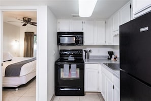 Una cocina compacta con armarios blancos, estufa negra, microondas y refrigerador.