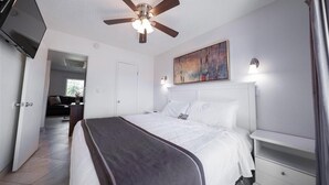 A hotel room with a bed, a ceiling fan, a TV, a painting, and a nightstand. - 215 Park Views, King Size Bed, Putting Green, Pickleball & More (Scottsdale)