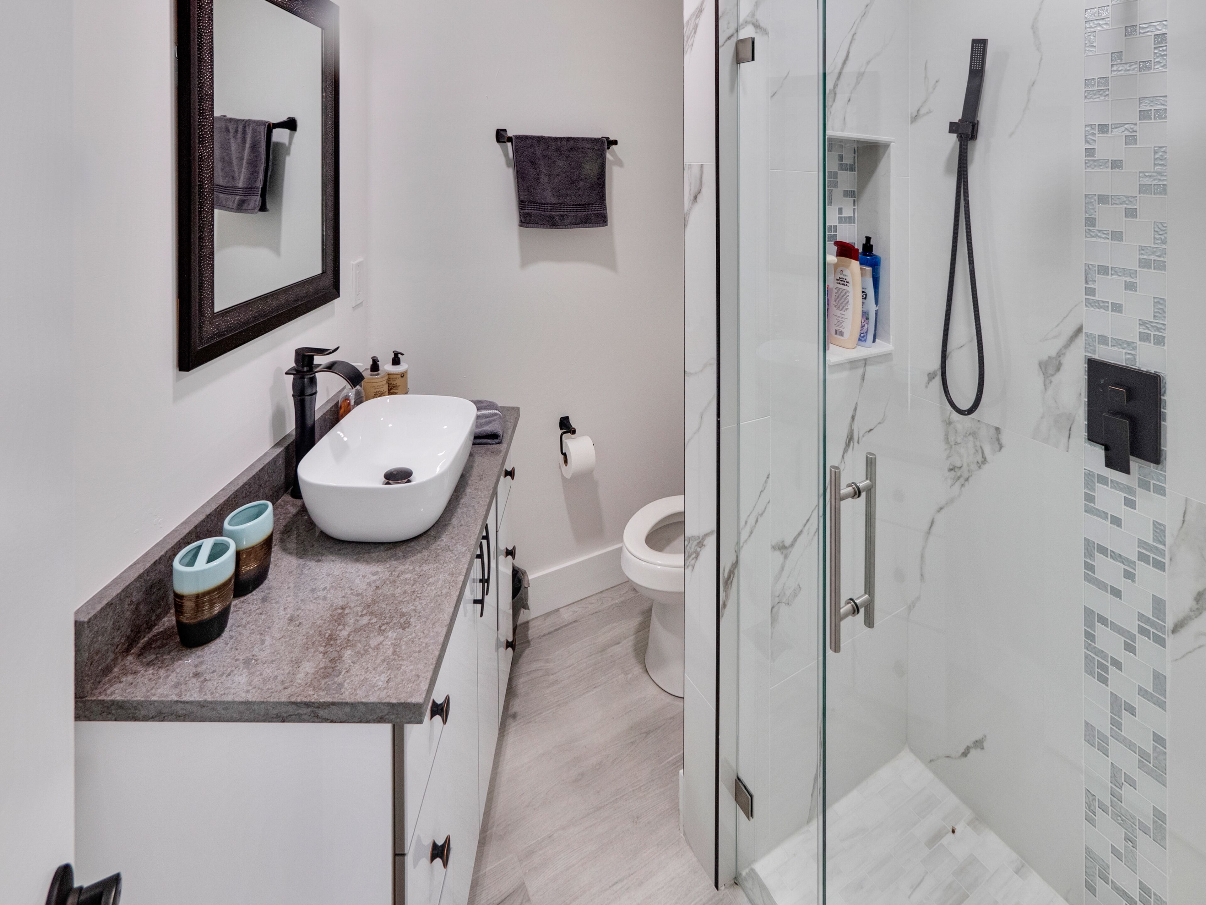 A modern bathroom with a white sink, marble backsplash, and a glass-enclosed shower.